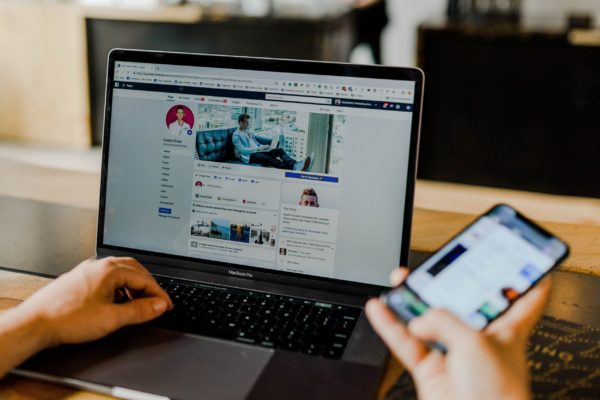 A person managing his small business social media page while holding his phone on his other hand.