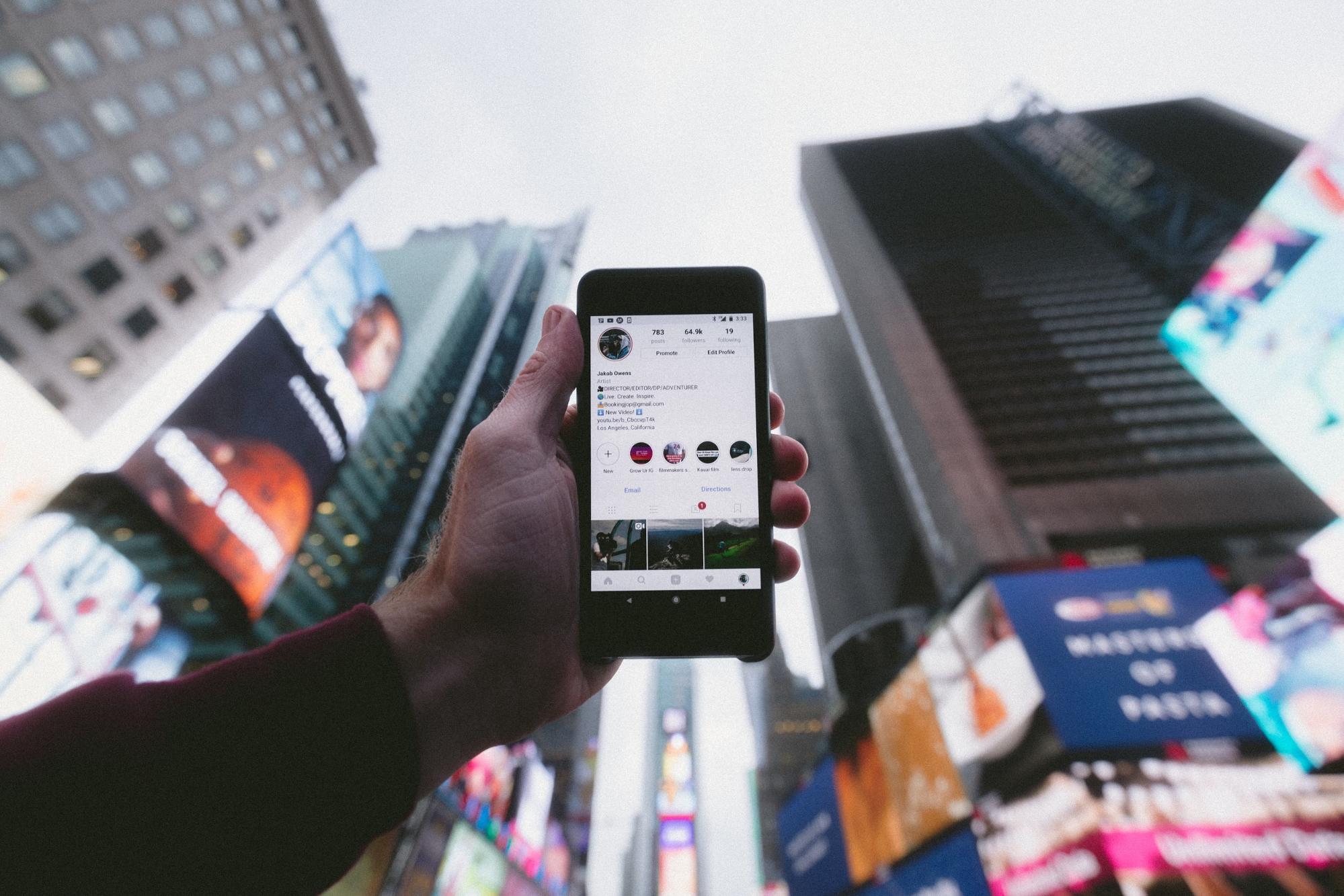 Hand holding phone up with high rise building in the background.